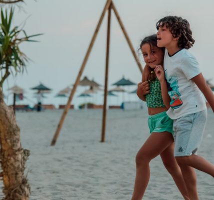 Two children enjoy a playful walk on a sandy beach, capturing summer fun.