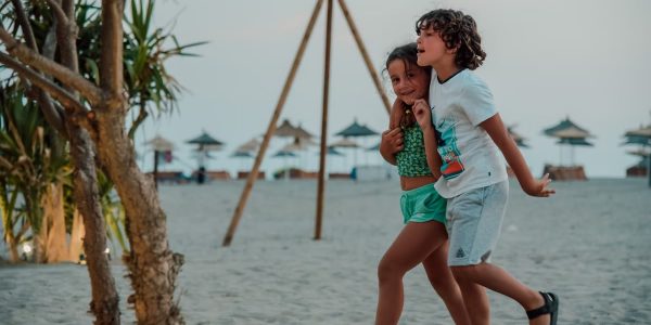 Two children enjoy a playful walk on a sandy beach, capturing summer fun.